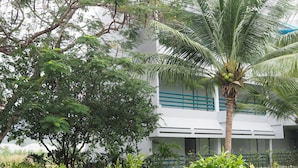 Un bâtiment à l’extérieur blanc, agrémenté de touches de bleu, entouré d’une végétation luxuriante comprenant un palmier et divers arbustes.