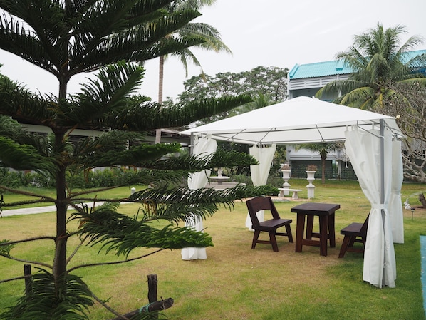 An outdoor seating area with a white canopy, wooden tables and chairs, and a small fountain.