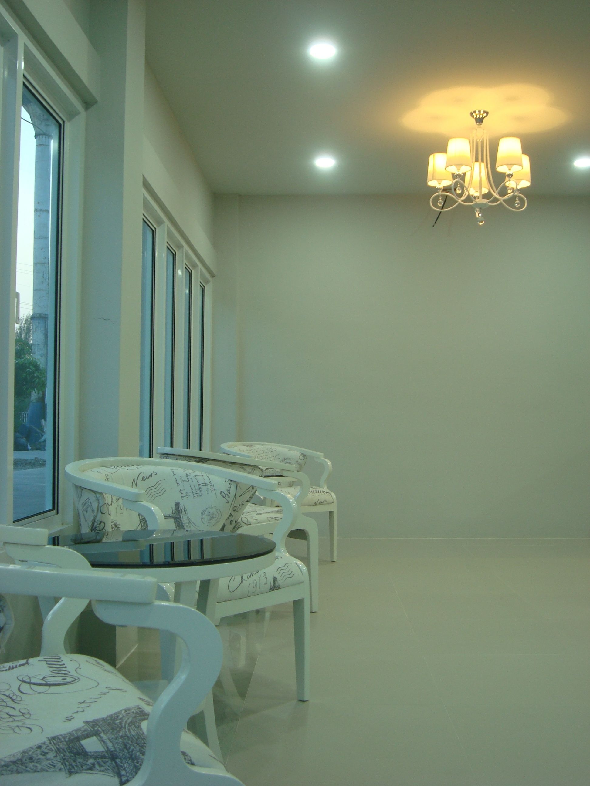 Una habitación con muebles blancos, una araña y ventanas amplias.