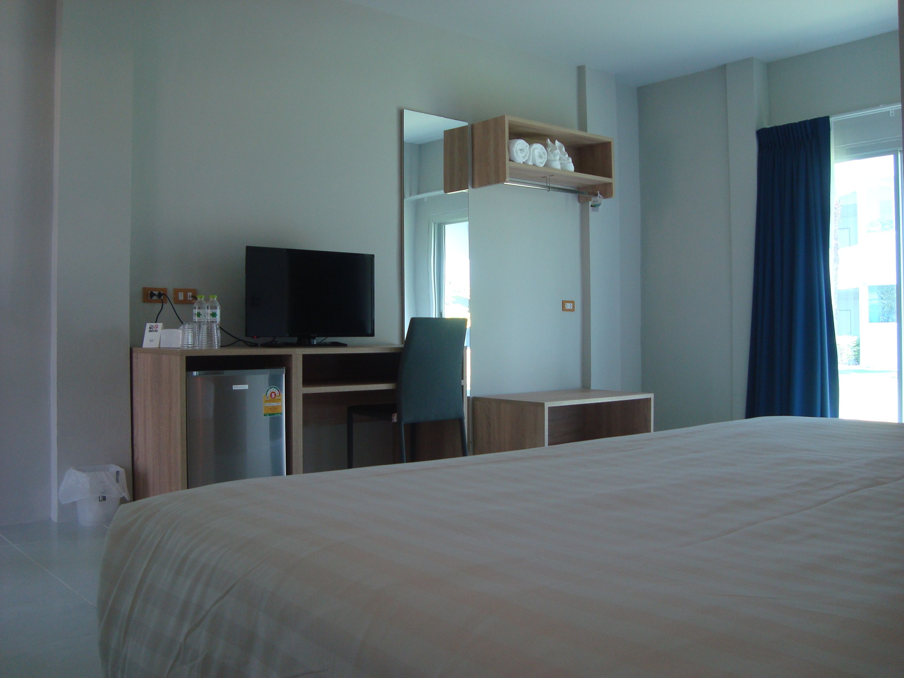 Habitación de hotel con cama, escritorio con televisor, una silla, refrigerador pequeño y estante con toallas.