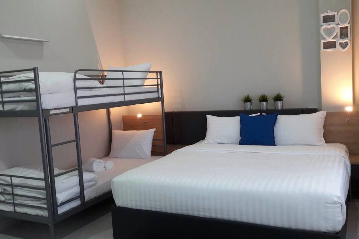 Een hotelkamer met een stapelbed, een enkel bed en een nachtkastje met een lamp.