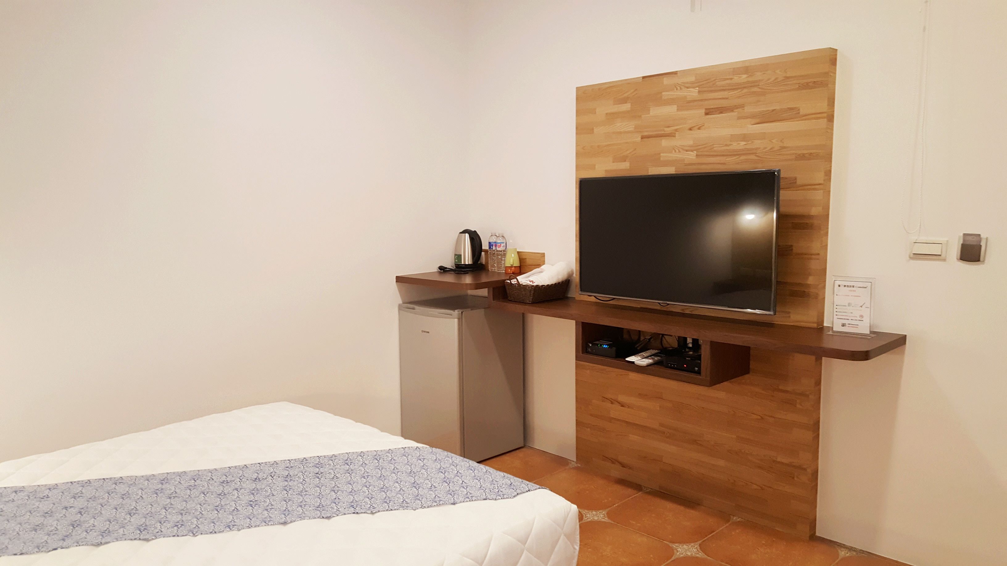 A hotel room with a bed, a small kitchenette, a TV mounted on a wooden wall, and a wooden floor.