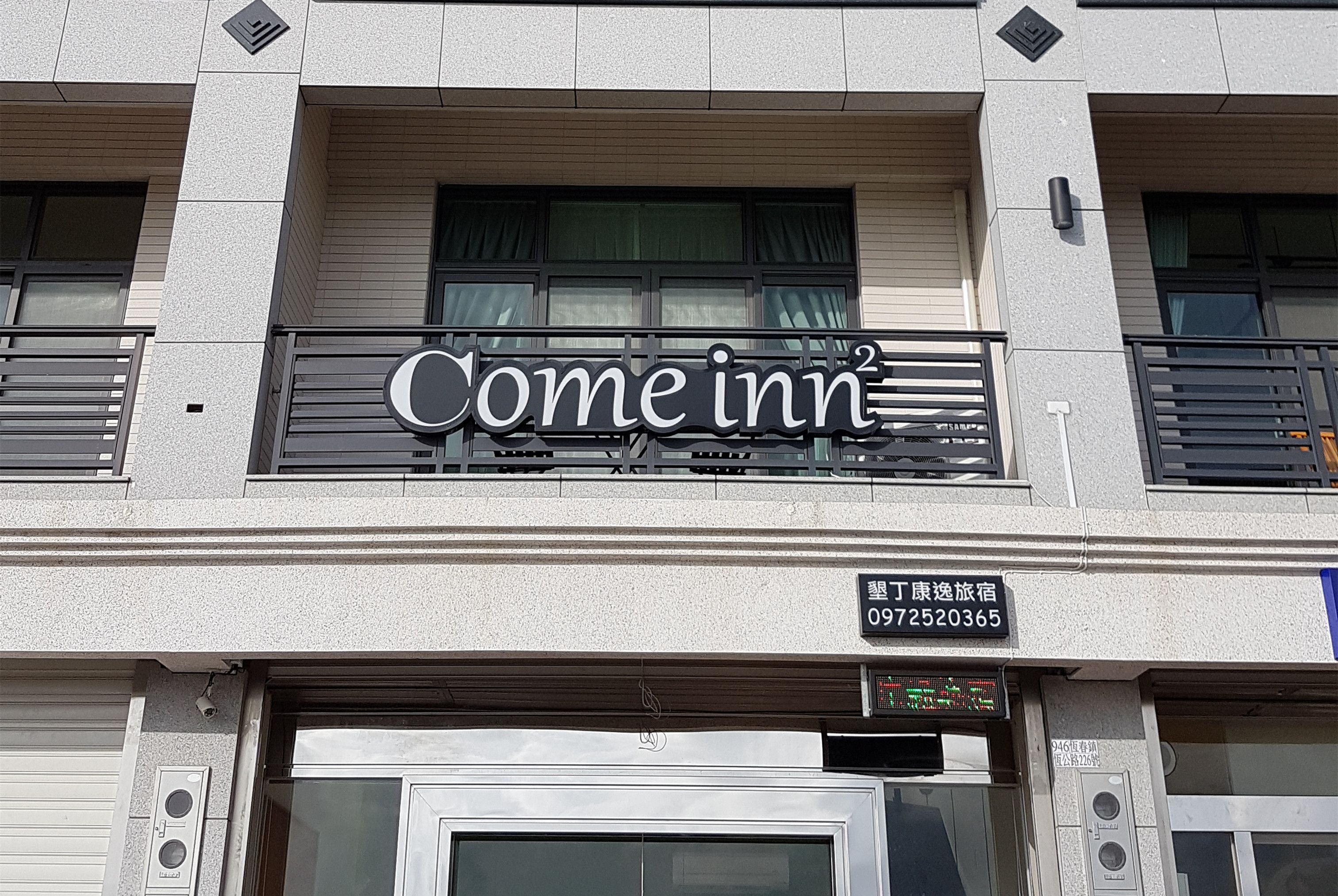 Fachada de hotel con un letrero que dice 'Come inn', un número de contacto y una pantalla digital.