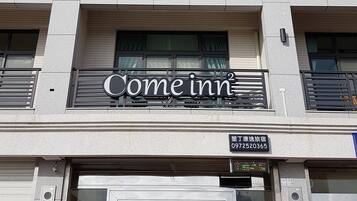 Een hotelgevel met een 'Come inn' bord, een telefoonnummer en een digitaal scherm.