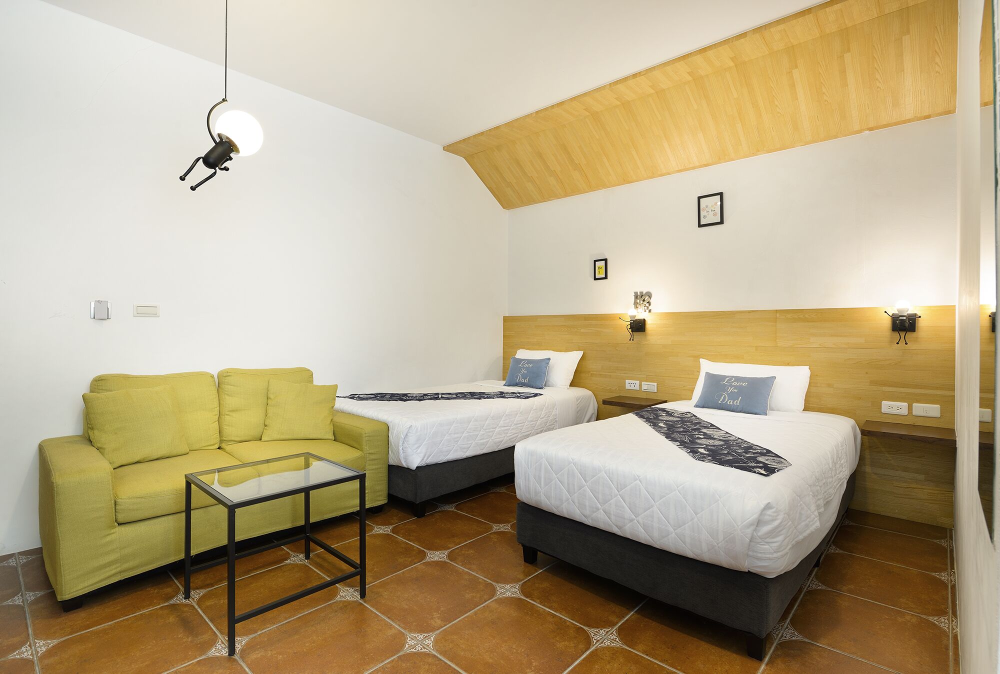 A hotel room with two beds, a sofa, a glass-top table, and a wooden ceiling.