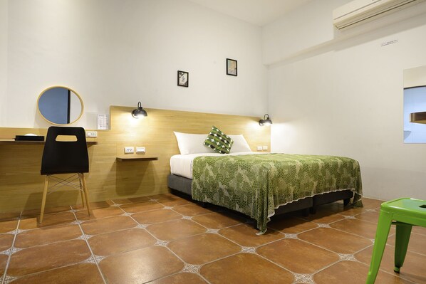 A hotel room with a bed, a desk with a chair, a green stool, and a wall-mounted air conditioner. - Come Inn 2 (Hengchun)