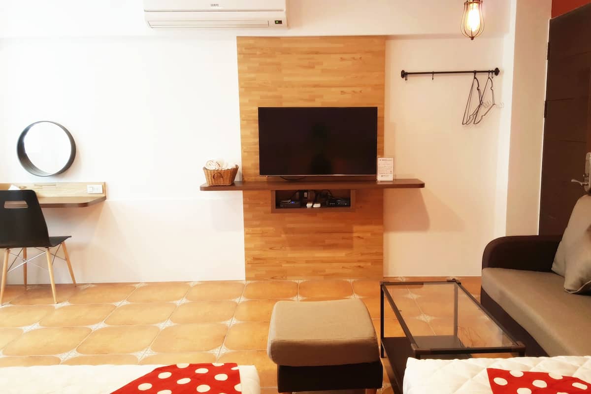A living room with a flat-screen TV mounted on a wooden wall, a black chair, a sofa with cushions, a glass coffee table, and a patterned rug.