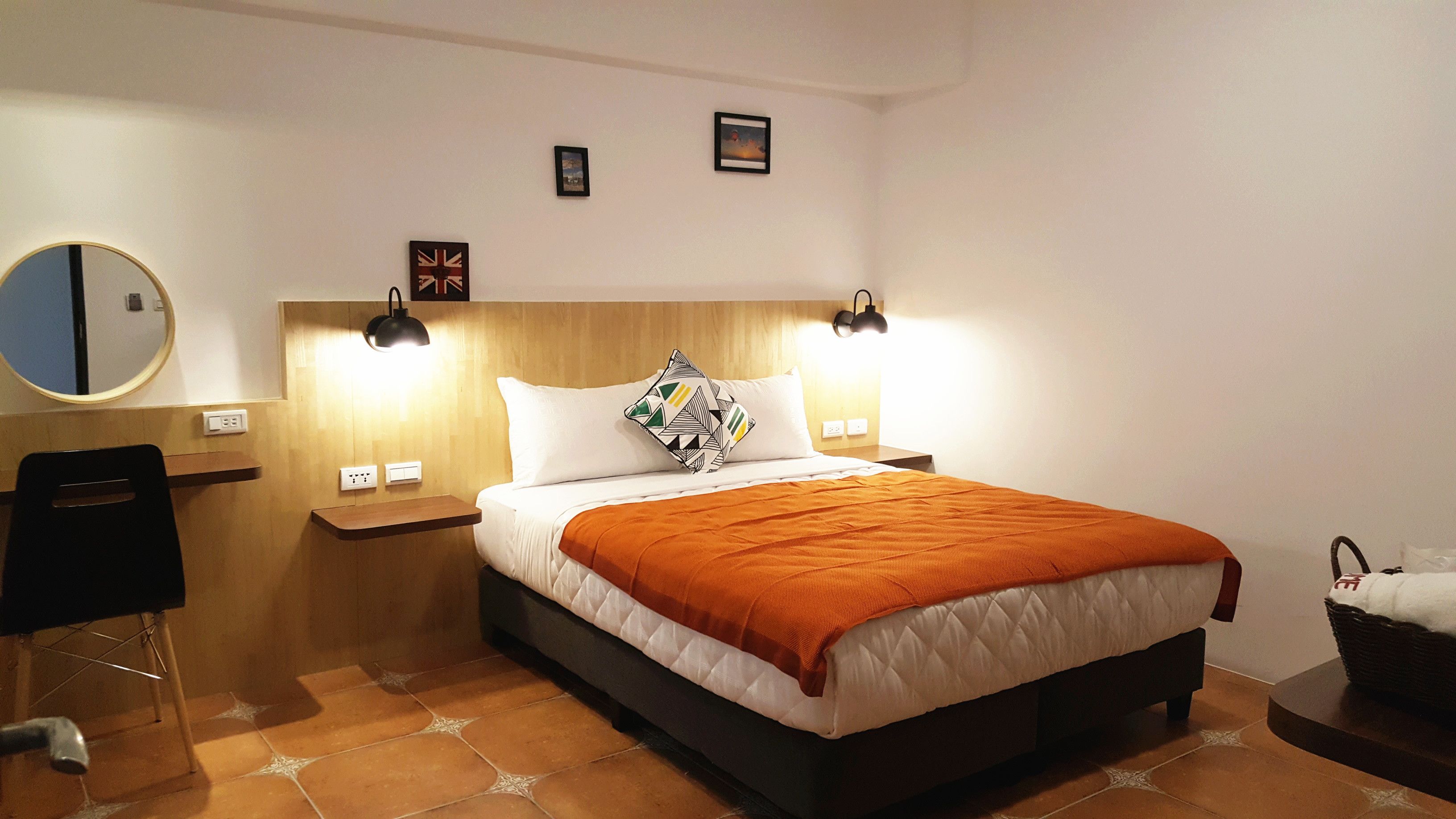A neatly arranged hotel room with a bed, bedside tables, a mirror, and a wall-mounted lamp.