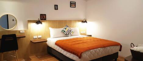 A neatly arranged hotel room with a bed, bedside tables, a mirror, and a wall-mounted lamp.