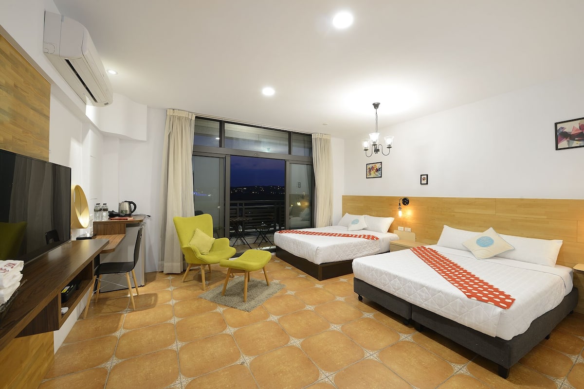 A hotel room with two beds, a desk, a chair, and a view of the city at night.