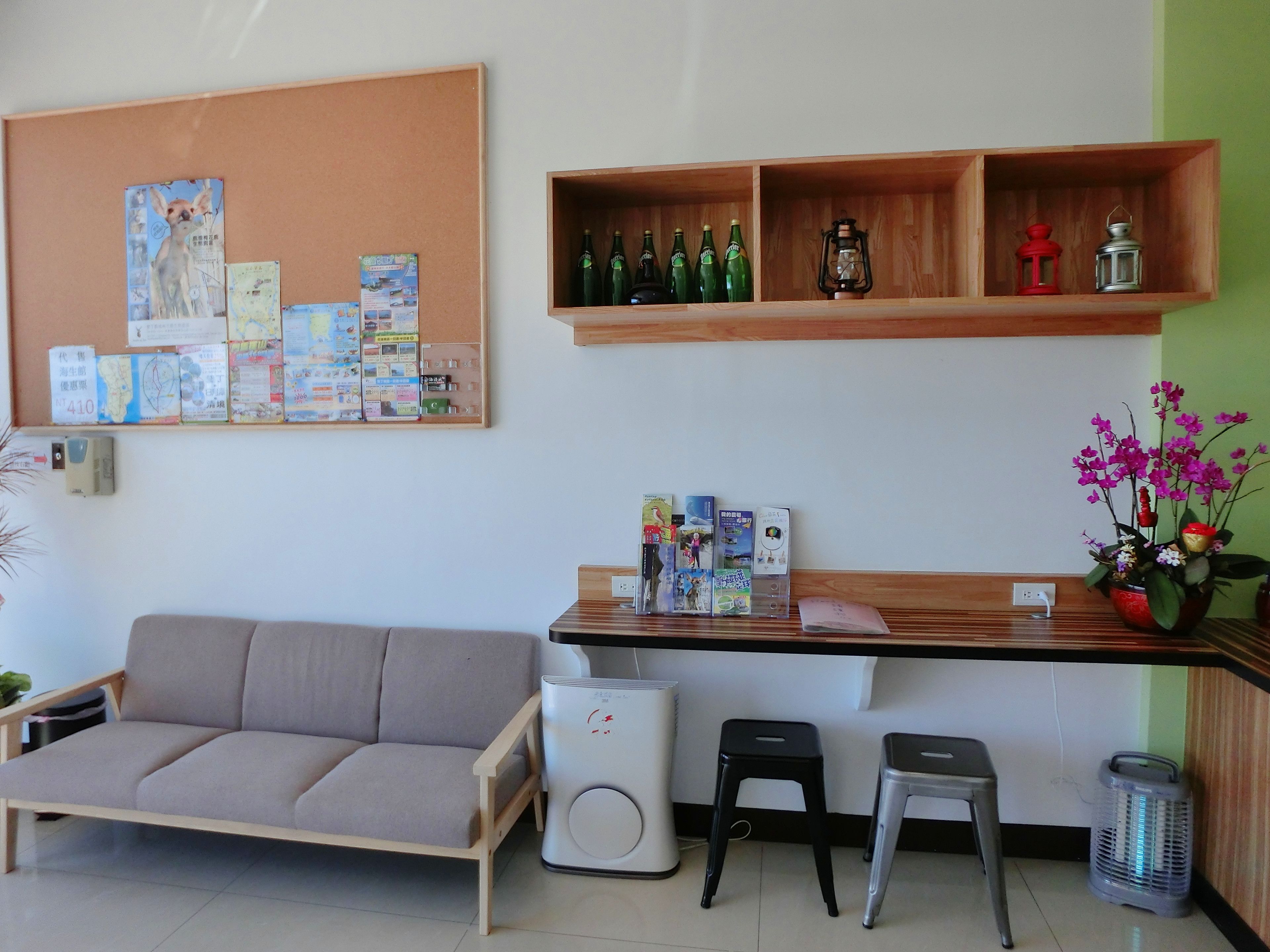 Un espace d’accueil comprenant un panneau d’affichage, un canapé, un comptoir avec des bouteilles et une lanterne, ainsi qu’une orchidée en pot.