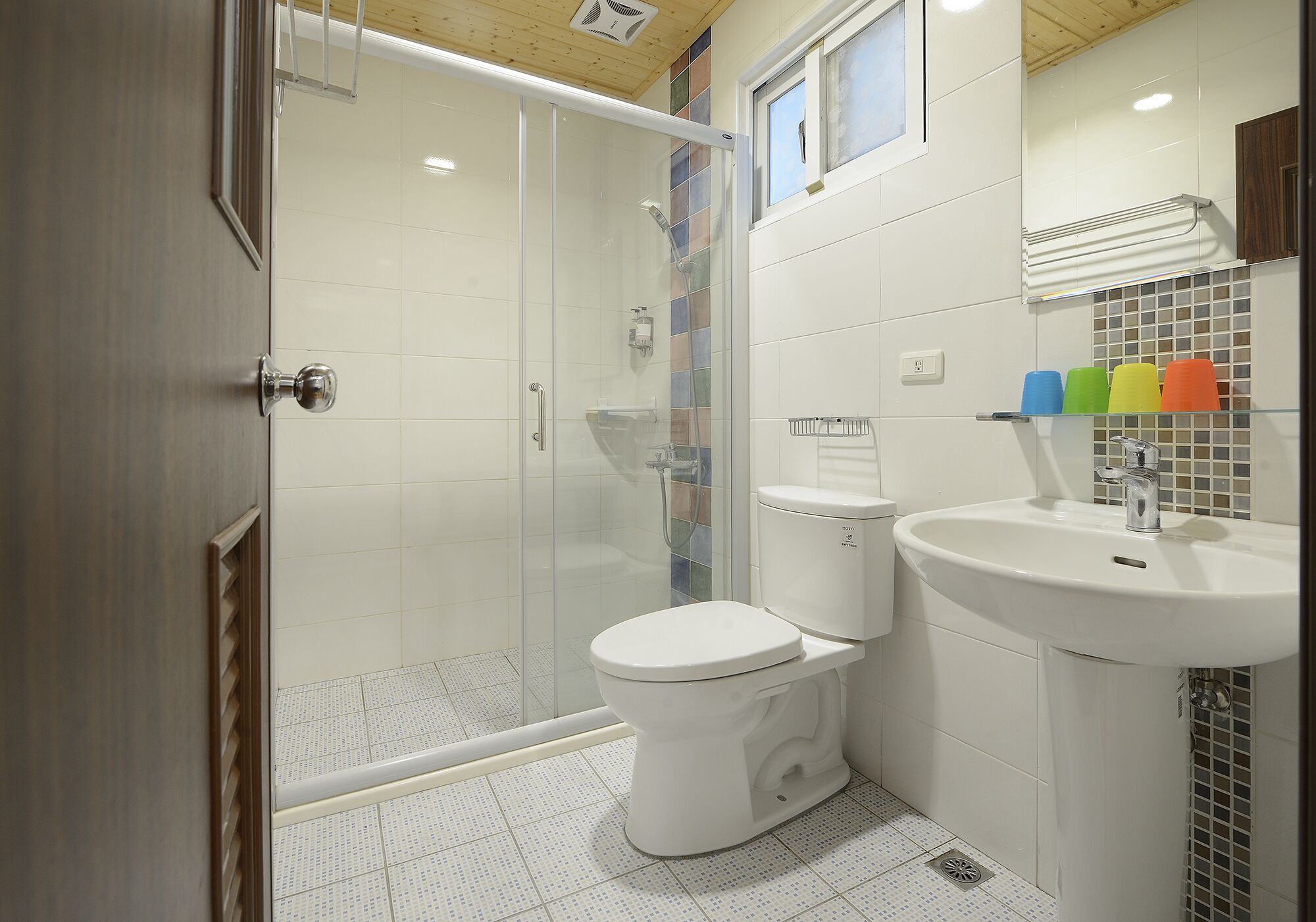 A modern bathroom with a glass-enclosed shower, a white toilet, and a sink with a mirror.