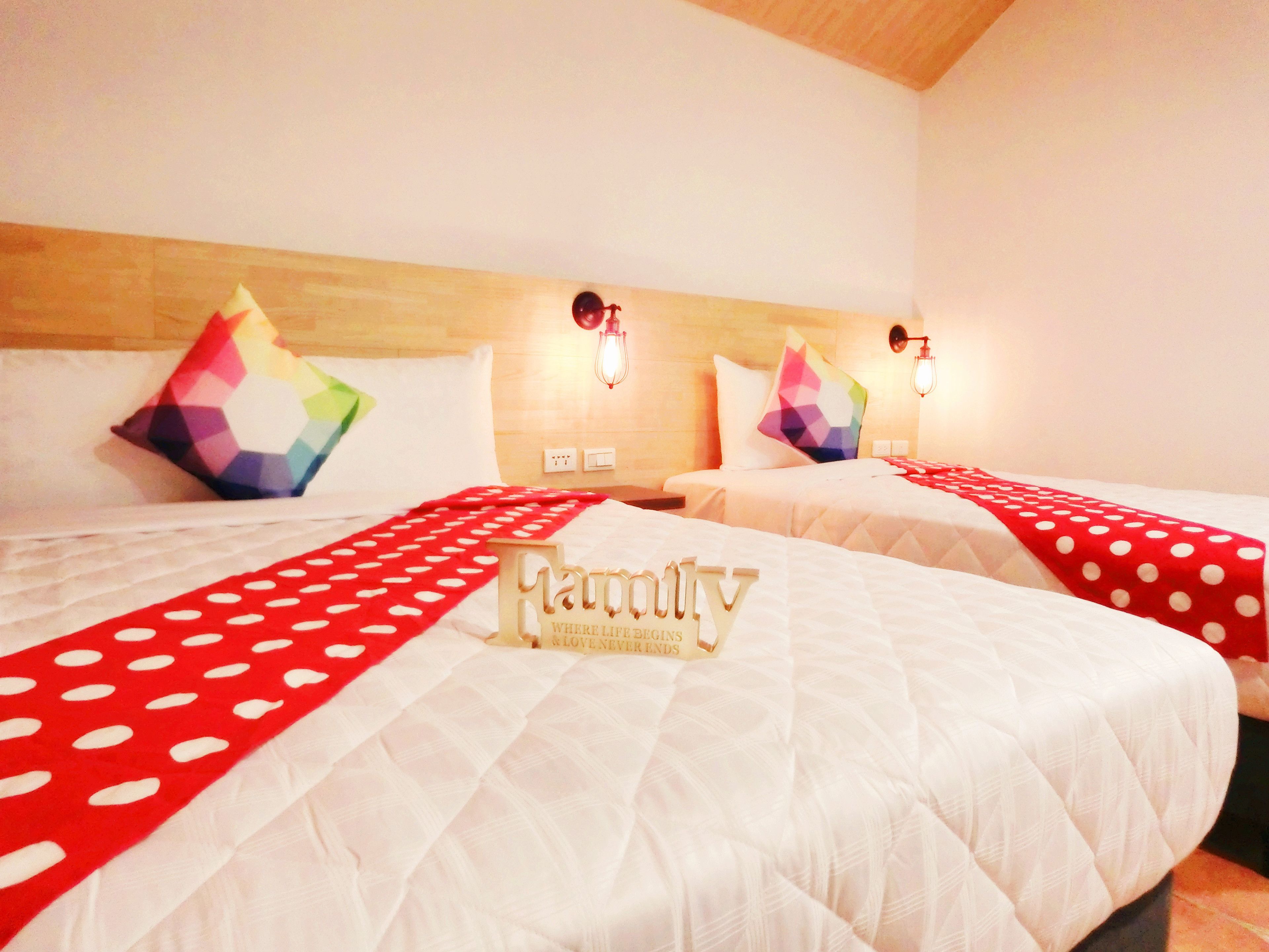 Une chambre d’hôtel avec deux lits, chacun recouvert d’une couverture à pois rouges, et une pancarte sur laquelle on peut lire : « Mandy, là où la vie commence et l’amour finit ».
