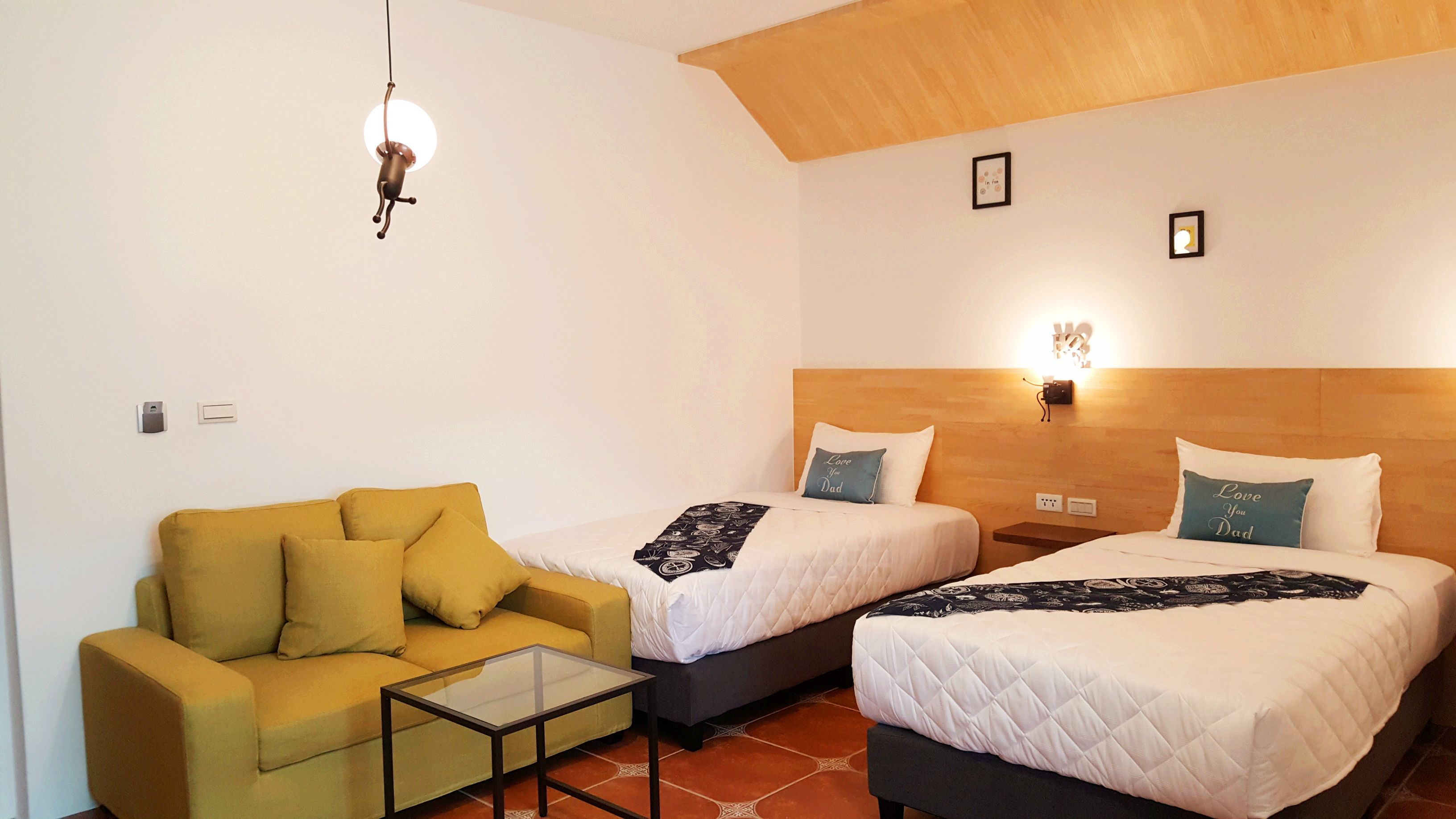 A hotel room with two beds, a sofa, a glass coffee table, and a wooden ceiling.