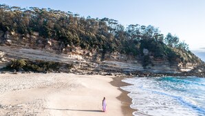 Una playa con una persona caminando por la orilla, vestida con un largo vestido.