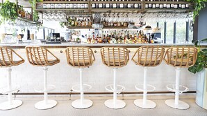 Una zona de bar con diversas opciones de asientos, incluyendo sillas y taburetes de mimbre, y una variedad de botellas y vasos en estantes.