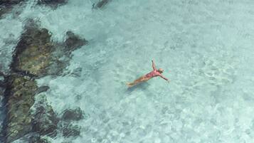 Una persona flotando en aguas transparentes cerca de rocas.