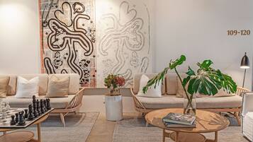 A modern living room with a sofa, coffee table, and a chessboard. There is a large abstract artwork on the wall and a plant on the coffee table.