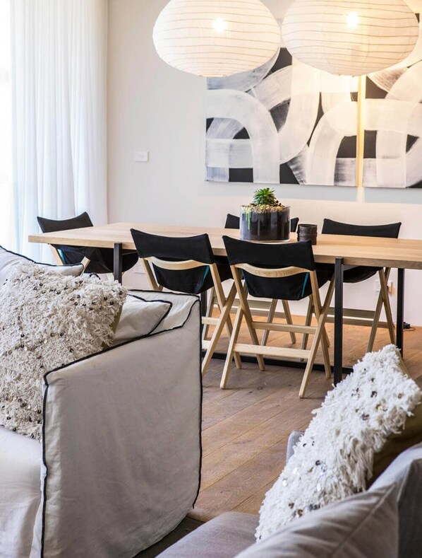 Un espace repas moderne avec une table en bois, des chaises noires et un grand tableau abstrait accroché au mur.