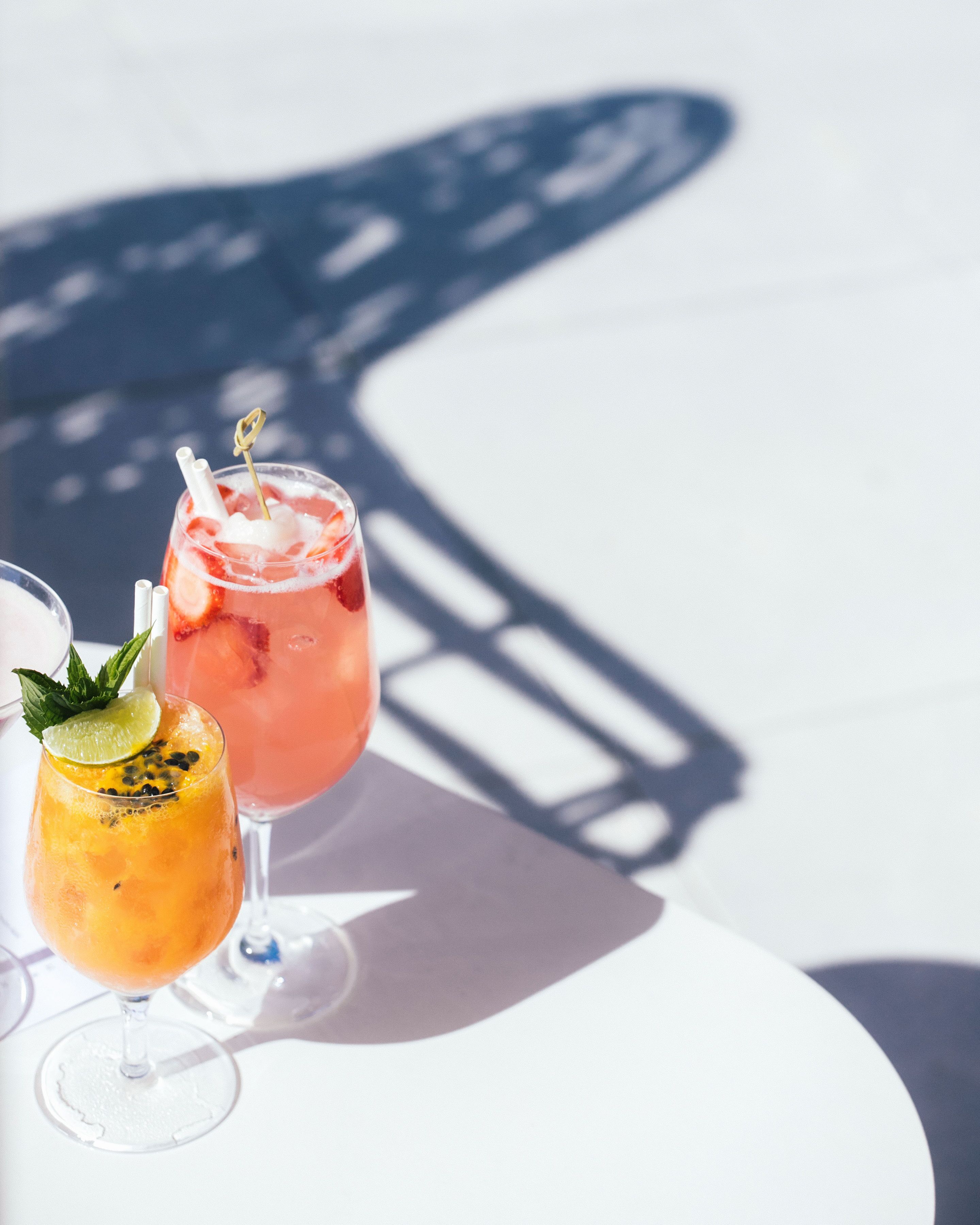 Due cocktail su un tavolo bianco, con l'ombra di una struttura.