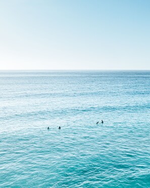 Vista ampla de um mar calmo com três surfistas ao longe.