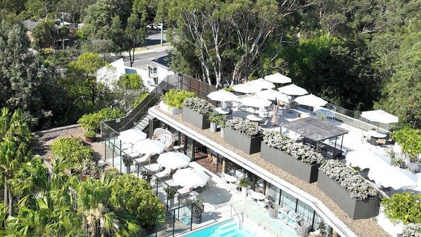 Un área de piscina en la azotea con sillones de descanso y sombrillas, rodeada de exuberante vegetación y vistas a un paisaje costero.