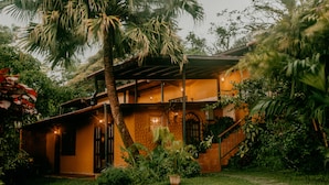 A two-story house with a covered patio, a staircase, and a garden with various plants. - The Golden Frog Inn (El Valle de Anton)