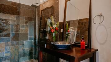 A bathroom with a glass shower enclosure, a wooden vanity with a blue basin, and a mirror.