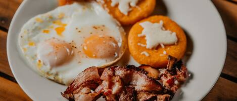 A plate with eggs, bacon, and a cup of coffee on a wooden table.