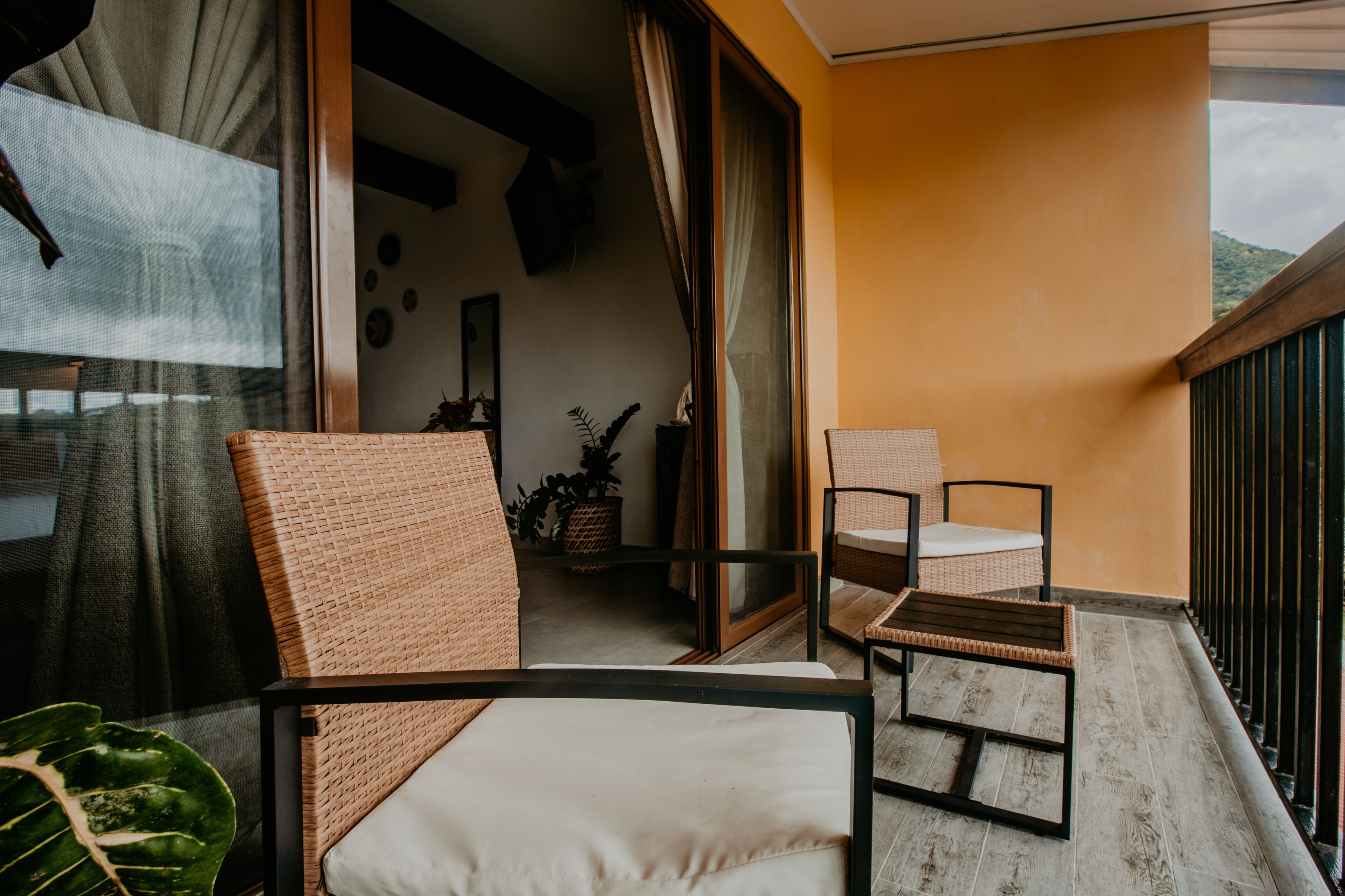 A balcony with wicker furniture, a potted plant, and a view of the outdoors.
