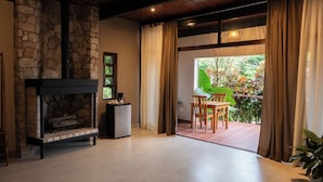 A cozy living room with a stone fireplace, a dining area with a table and chairs, and a view of greenery through large sliding doors. - The Golden Frog Inn (El Valle de Anton)