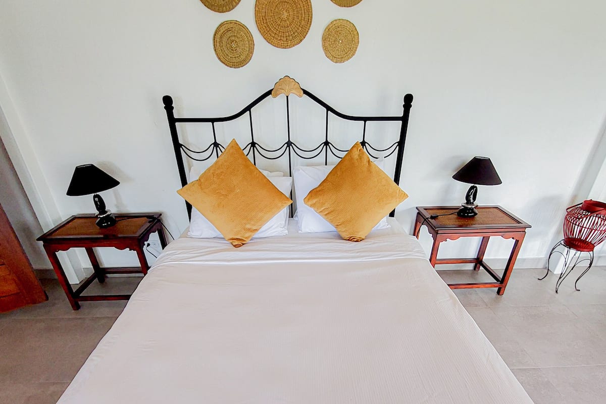 A neatly made bed with two pillows, a headboard with a decorative pattern, and two bedside tables with lamps.
