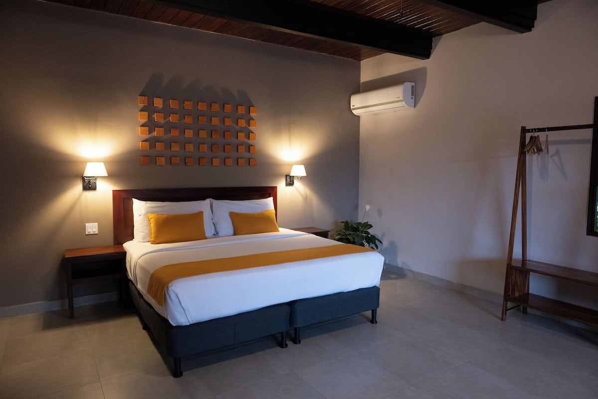 A neatly arranged bedroom with a large bed, two bedside tables, a wall-mounted light fixture, and a hanging rack.