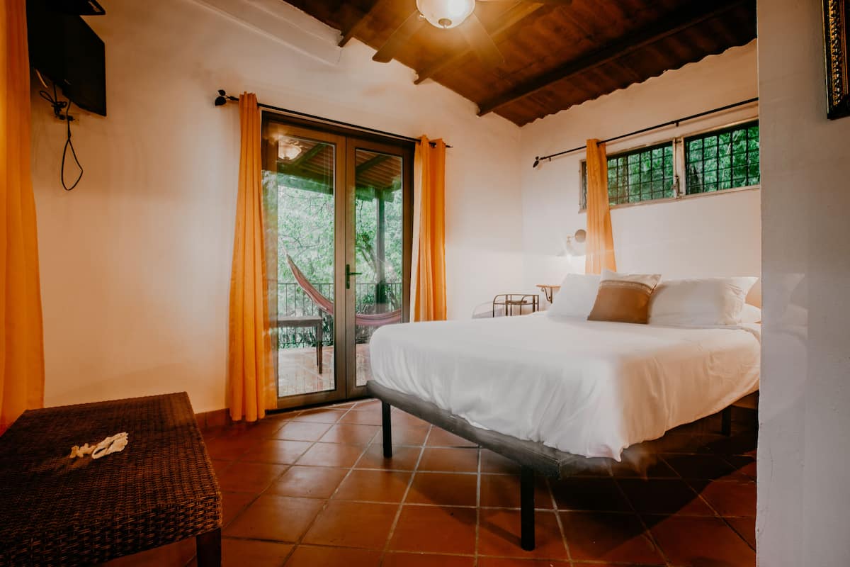 A bedroom with a bed, a small table, and a window with curtains.