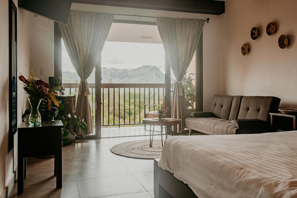 A bedroom with a bed, a sofa, a small table, and a view of mountains through large windows.