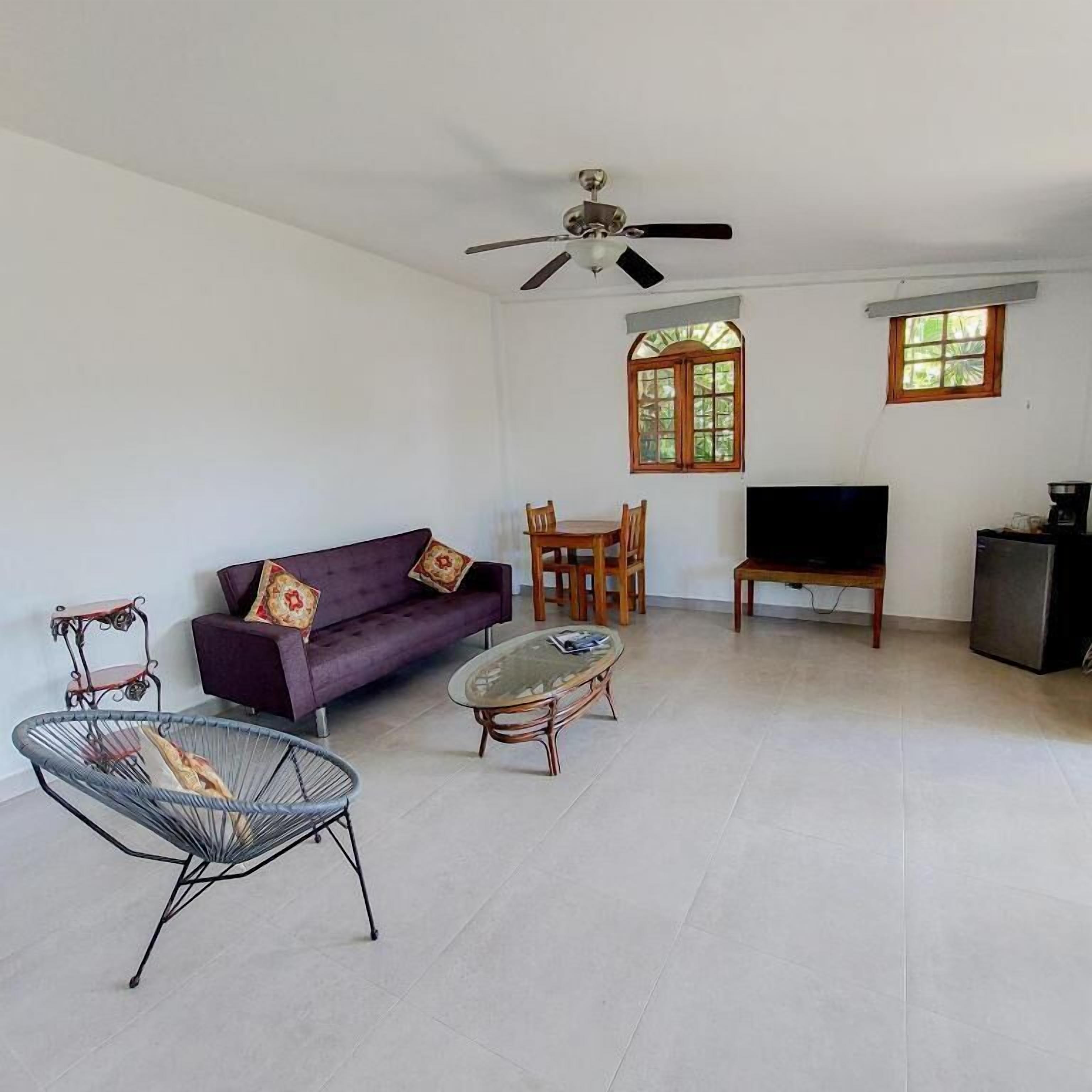 A living room with a sofa, a coffee table, a chair, a TV, and a ceiling fan.