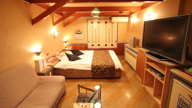 A hotel room with a bed, a TV, a sofa, and a desk with a lamp. - HOTEL DRESSY -Adults Only (Himeji)