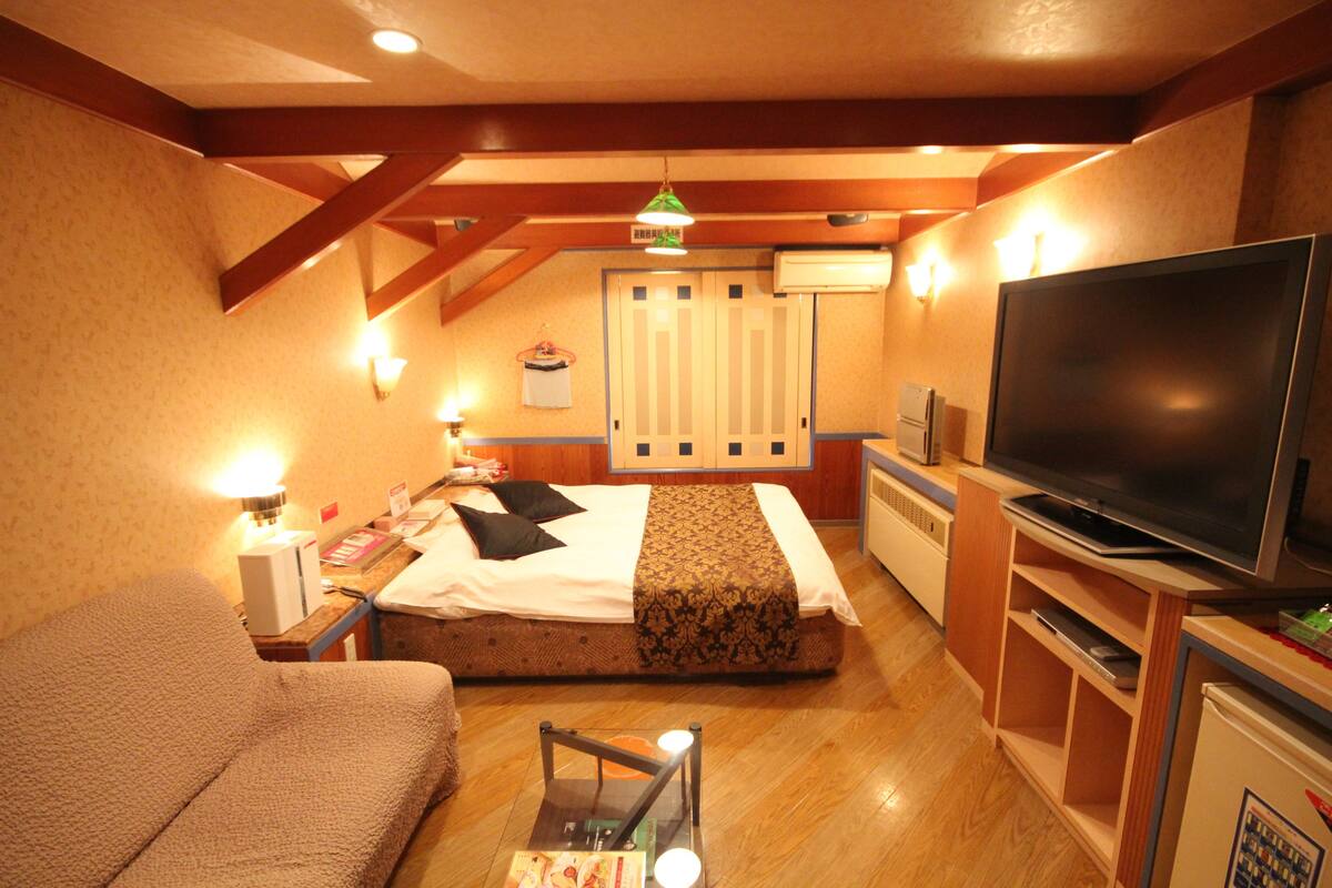 A hotel room with a bed, a TV, a sofa, and a desk with a lamp.