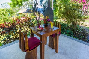 A wooden table with a placemat, a plate of fruit, a glass of yellow drink, and a potted plant. - TOYABALI - Resort (Tulamben)
