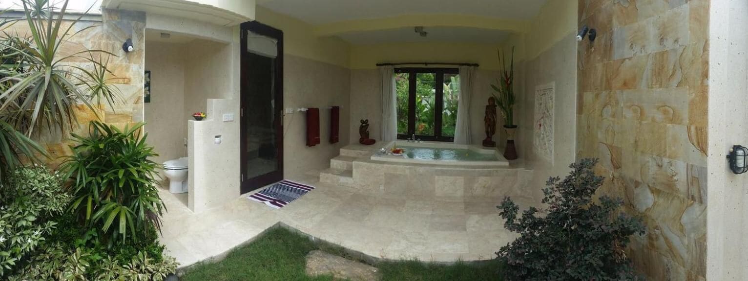 Een badkamer met een bad, douche en toilet. Er is een kleine tuin met planten en een deur naar buiten.