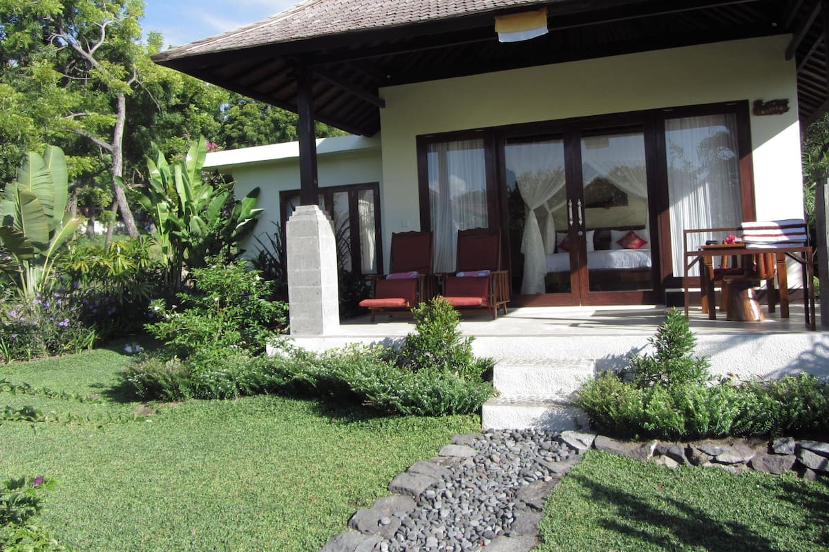 A house with a covered porch, a garden with various plants, and a bed with a canopy.