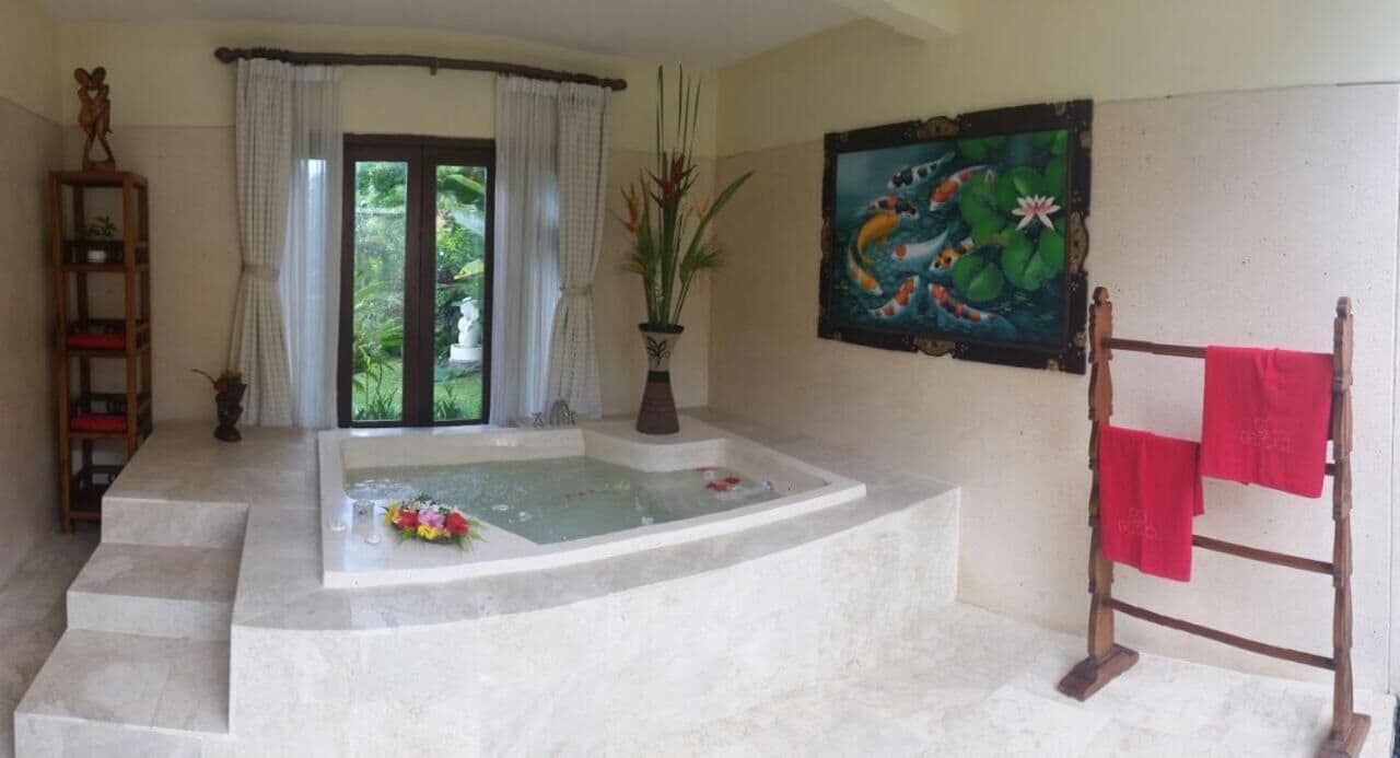 Un baño con bañera, ducha, escalera de madera con una toalla roja, estante con una planta y un cuadro de peces y nenúfares en la pared.