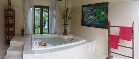 Un baño con bañera, ducha, escalera de madera con una toalla roja, estante con una planta y un cuadro de peces y nenúfares en la pared.