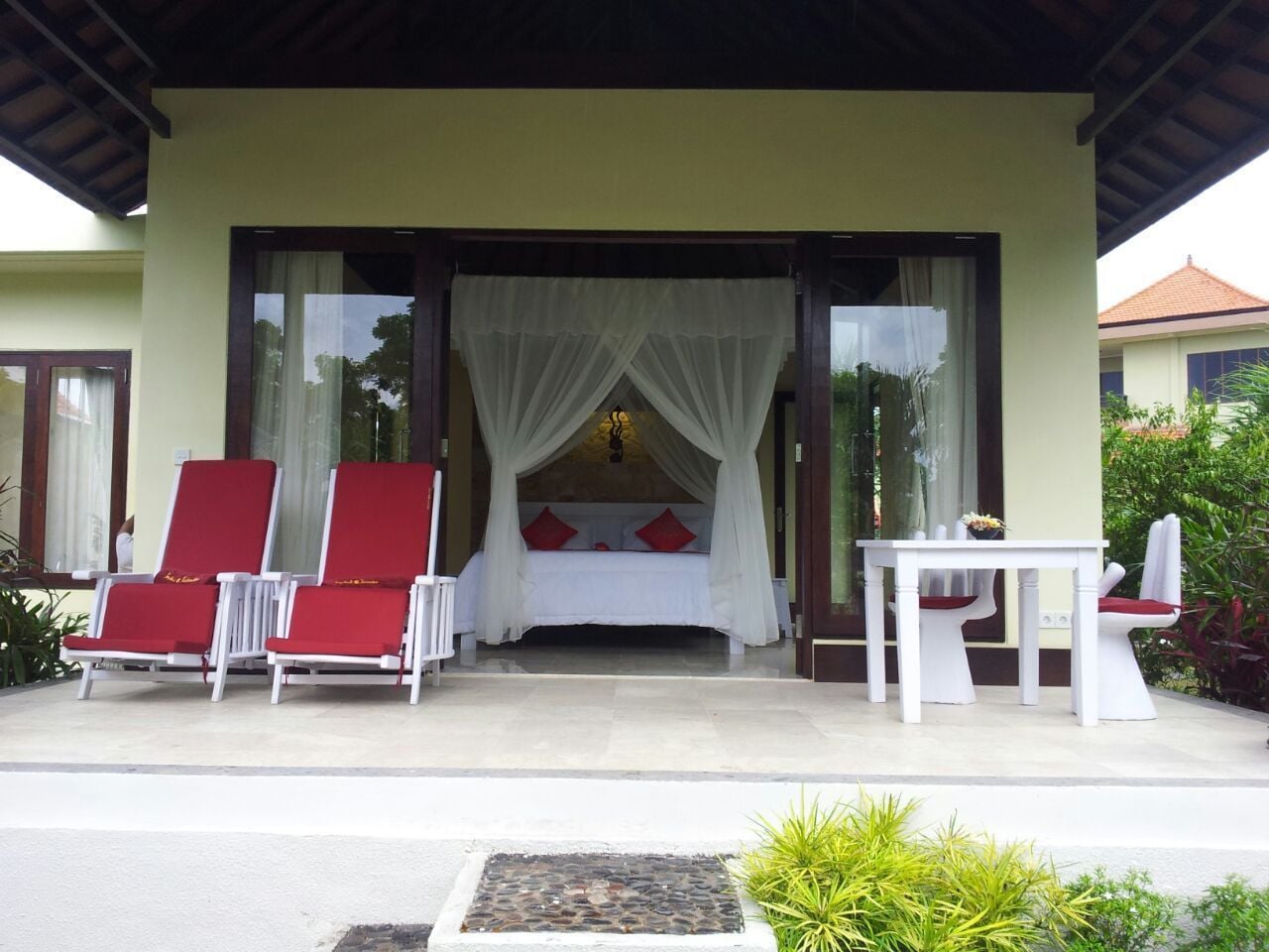 A room with a bed, two red lounge chairs, a table, and a canopy bed.
