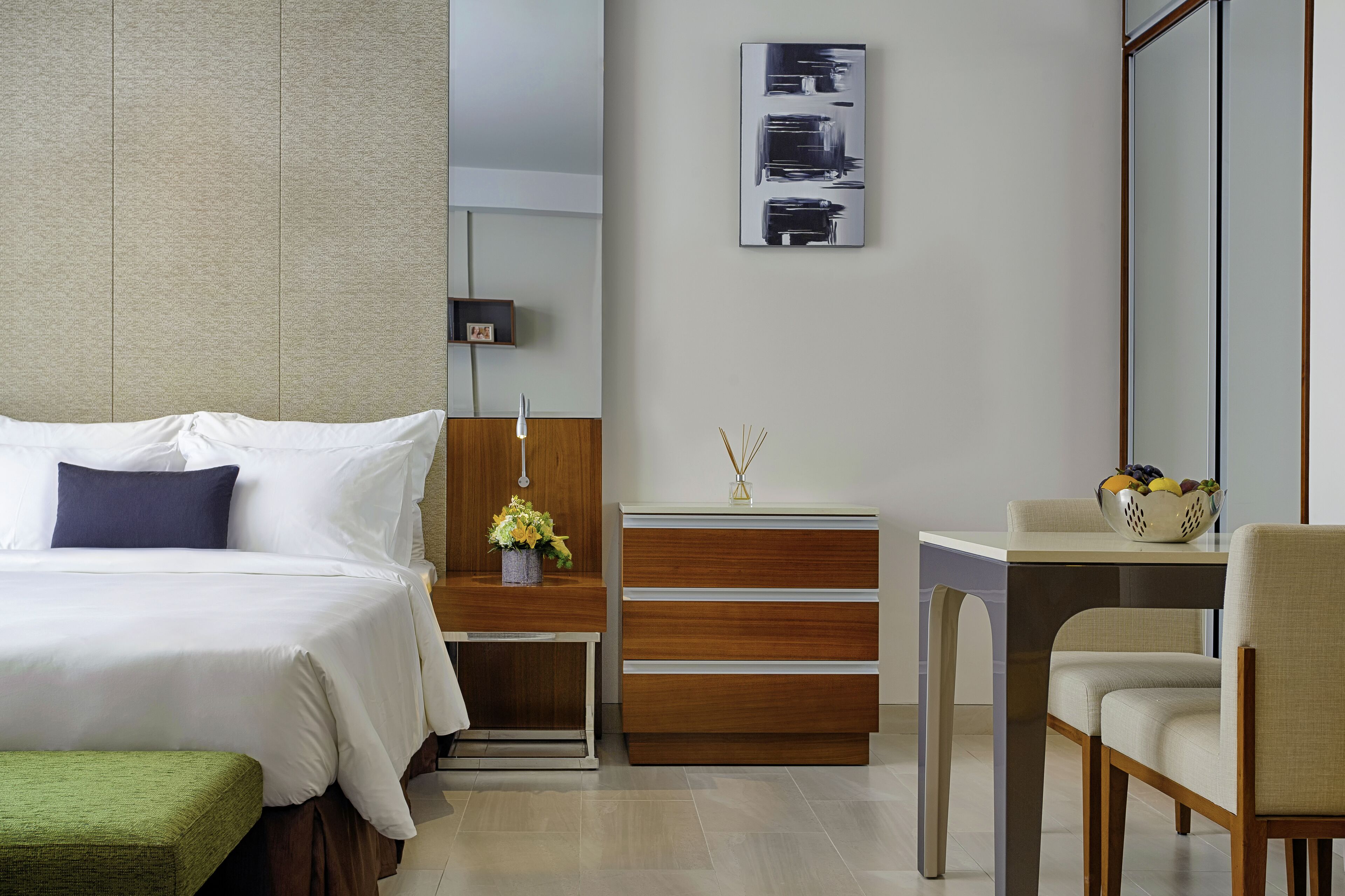 Habitació d'hotel moderna amb un llit ben fet, un taulell de fusta, una taula petita amb un ram de flors i una cadira.