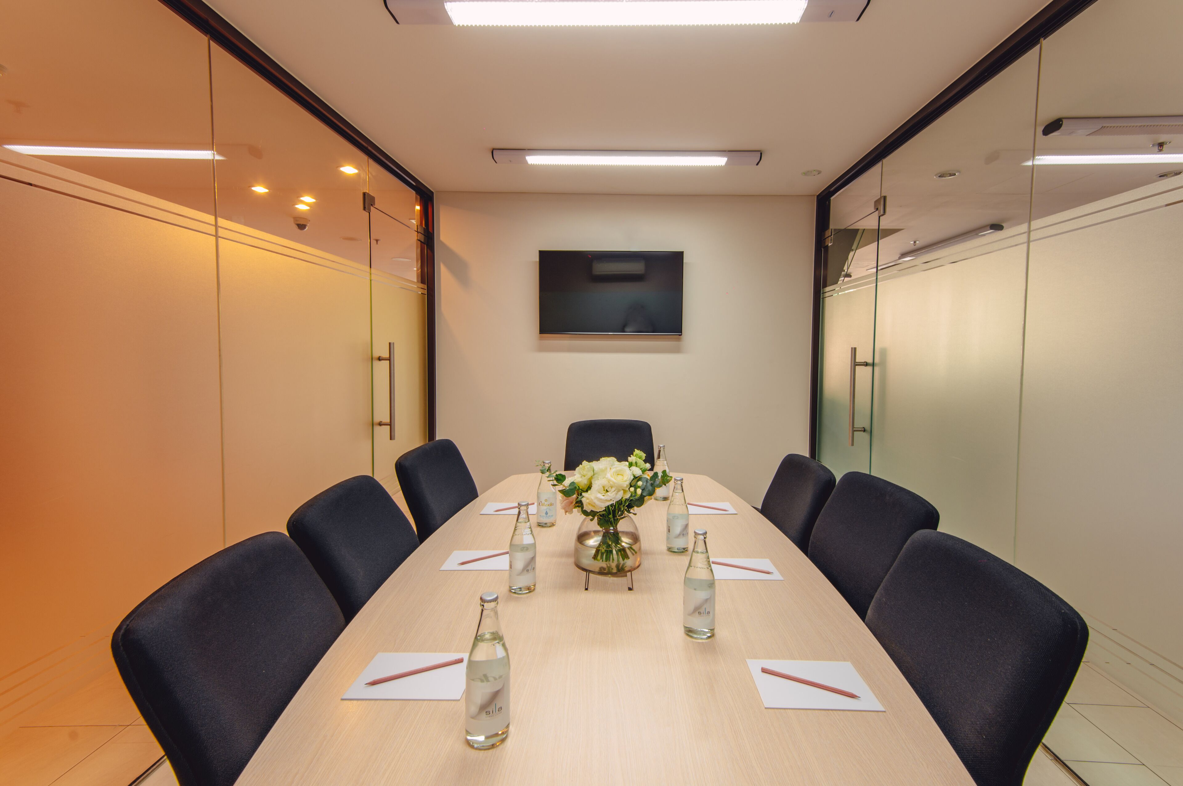 A conference room with a long table, chairs, a vase with flowers, and water bottles.