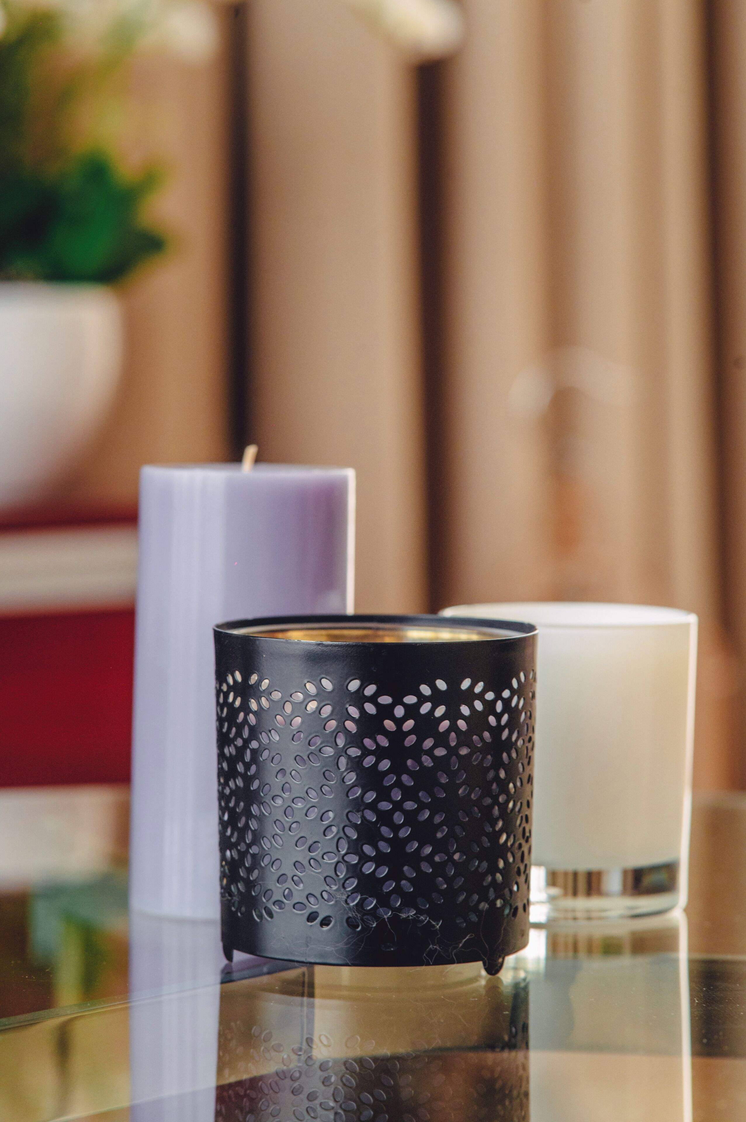 A table with three candles of different colors and a black candle holder with a textured pattern.