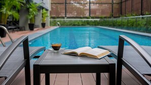 A poolside setting with a table, a book, and a cup of coffee.