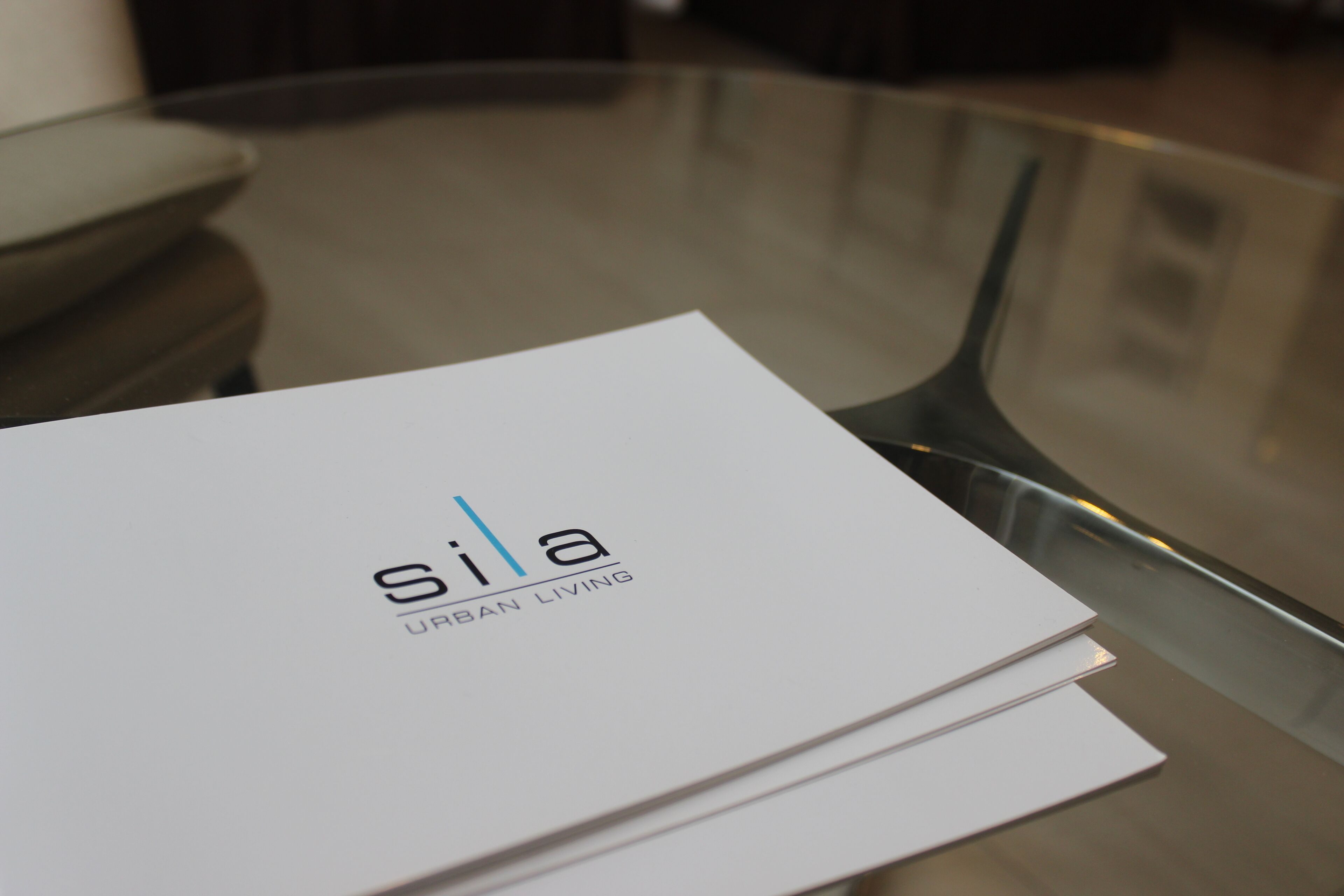 A white booklet with the text "Sila Urban Living" on a glass table.