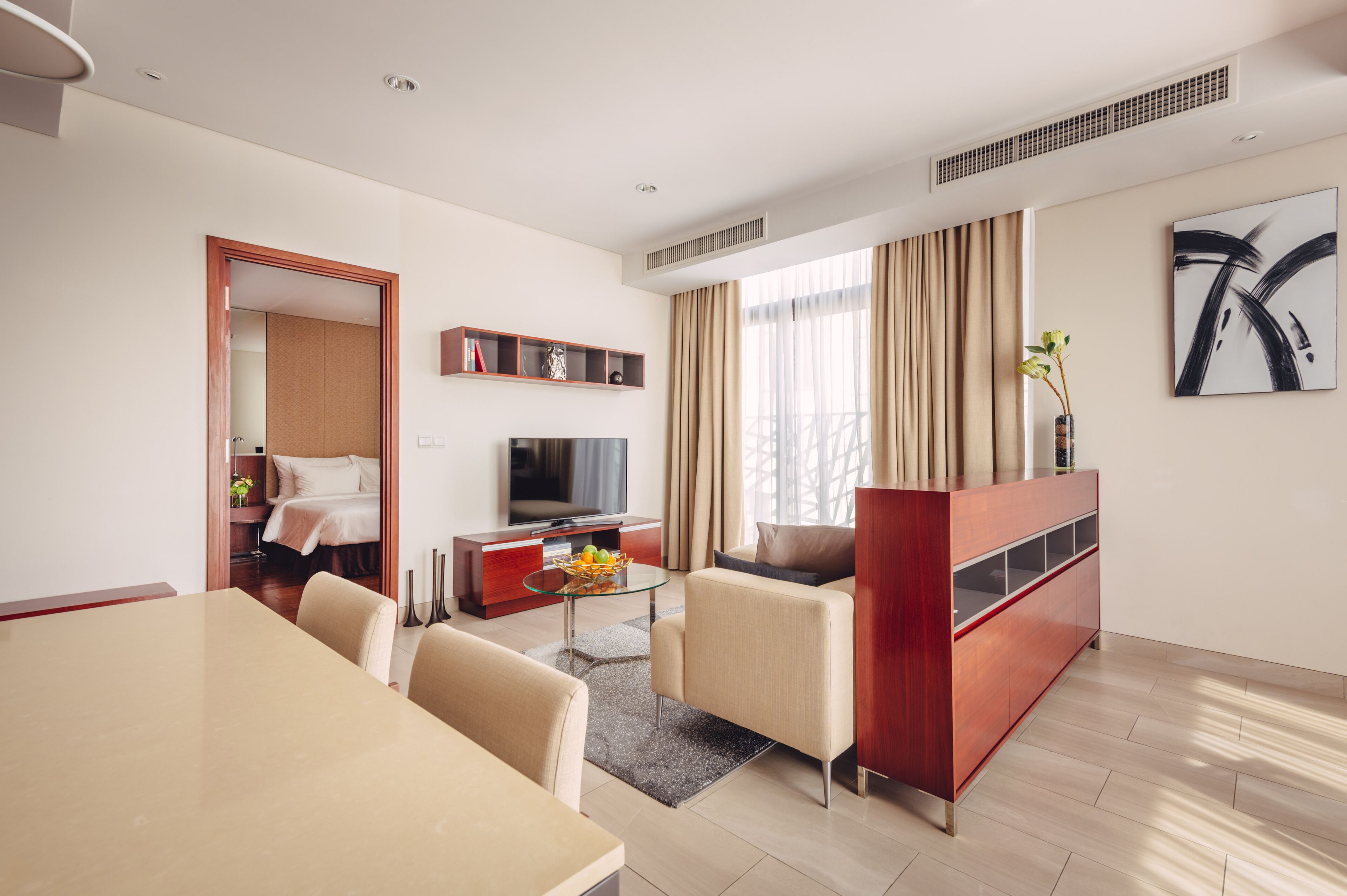 Une chambre d’hôtel moderne dotée d’un coin repas, d’une télévision, d’un canapé et d’une grande fenêtre avec des rideaux.